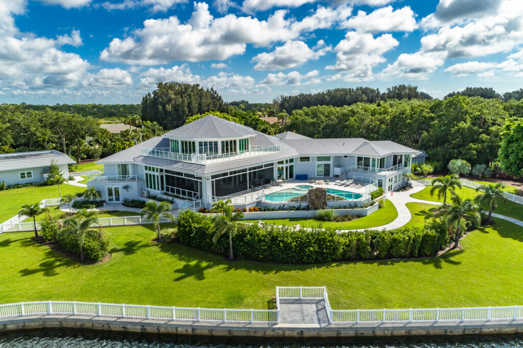 A photo of a white house with a pool and manicured lawns with trees in the background and a cloudy sky above.